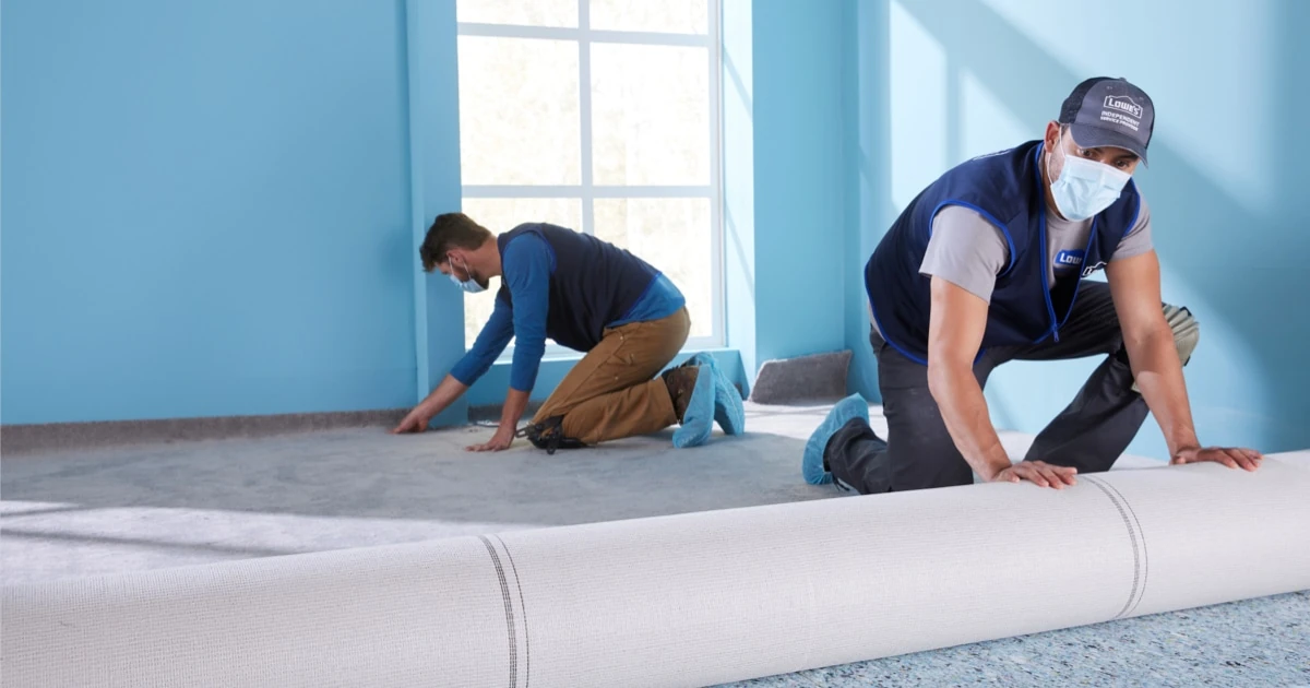 Two workers placing carpet in a room
