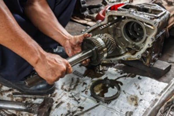 Hands working beside an opened transmission assembly on a workshop bench